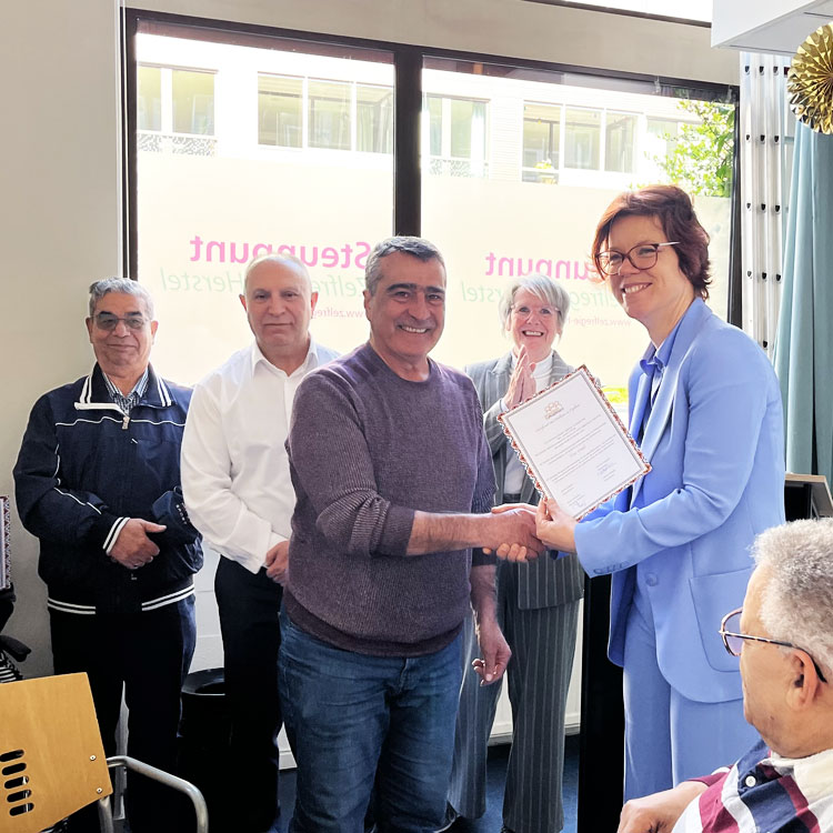 Een dame reikt een diploma uit aan een deelnemer van een samenwerkingsproject.