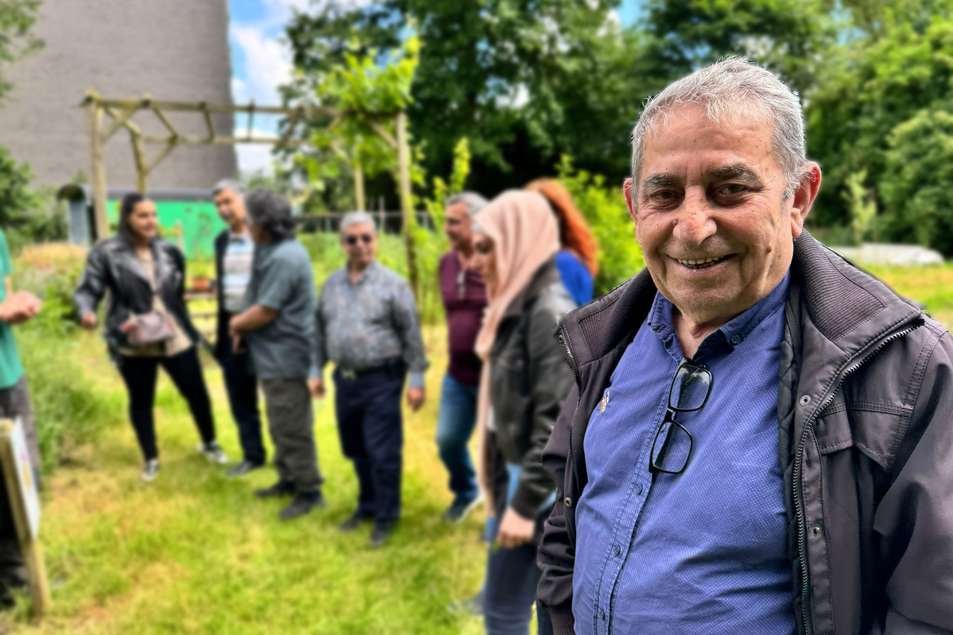 Een groep mannen en vrouwen gezellig aan het babbelen in een tuin.